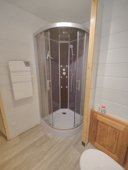 Douche moderne dans la salle de bains de l'appartement du Lauzet-Ubaye avec carrelage blanc et accents en bois
