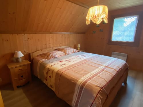 Chambre cosy en bois aux Gîtes Des Planchettes avec lit queen-size, table de nuit, TV écran plat et suspension décorative