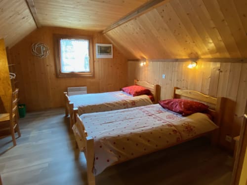 Chambre chaleureuse du chalet en bois des Gîtes Des Planchettes avec deux lits jumeaux, mobilier en pin et lucarne à Marigny