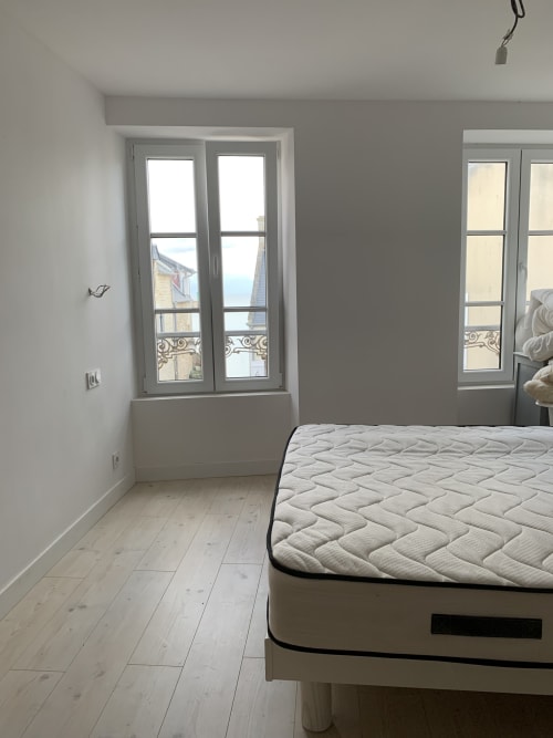 Bright bedroom at Les Filles du Bord de Mer with sea view, mattress, wood floors, and French doors overlooking harbor