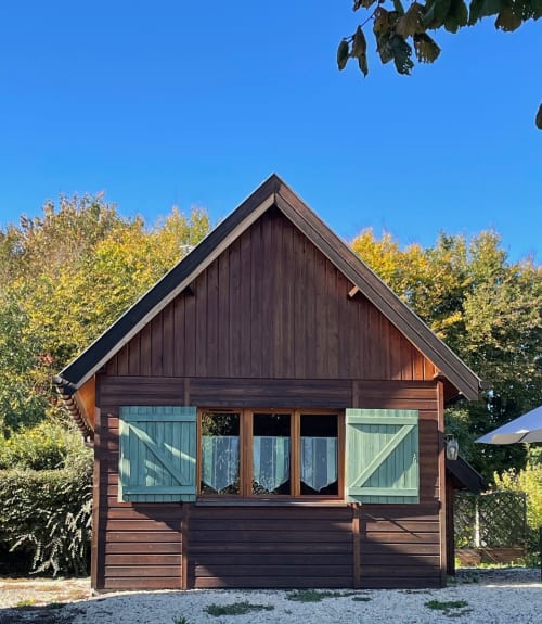Le chalet Rainette aux Gîtes Les Rainettes à Vienne-en-Bessin, avec sa façade en bois foncé et volets verts