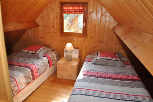 Chambre cosy de chalet en bois avec lits jumeaux, accents à carreaux rouges et vue sur le jardin aux Gîtes Les Rainettes