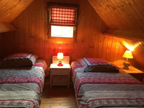 Chambre douillette au Gîtes Les Rainettes avec deux lits, literie à carreaux rouges et éclairage chaleureux