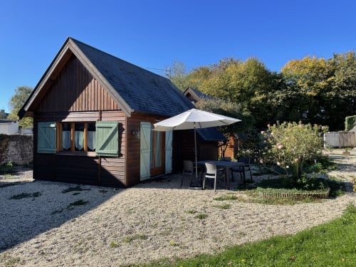 Chaumière moderne aux murs en bois sombre, toit pointu et parasol blanc aux Gîtes Les Rainettes, Vienne-en-Bessin