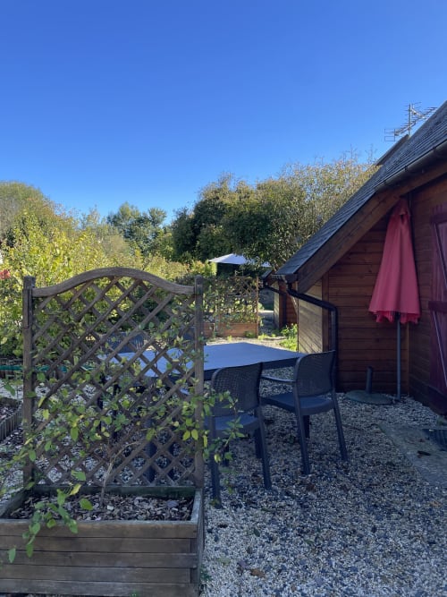 Patio du gîte Les Rainettes avec portillon à treillage, table, chaises et parasol bordeaux sous ciel dégagé