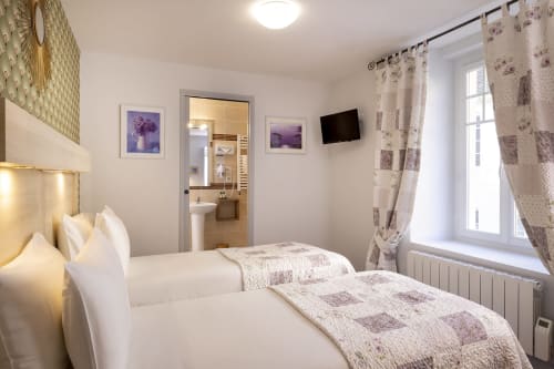Chambre twin lumineuse à l'Hôtel De Lion Sur Mer avec lits blancs, salle de bains privée, TV écran plat et rideaux fleuris