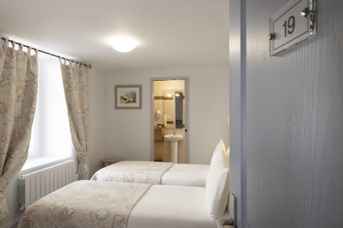 Chambre twin standard à l'Hôtel De Lion Sur Mer avec deux lits, salle de bains privée, fenêtre aux rideaux fleuris et décor moderne