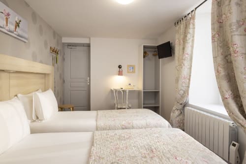Chambre Twin lumineuse à l'Hôtel De Lion Sur Mer avec deux lits, rideaux fleuris, bureau, télévision écran plat et vue fenêtre sur