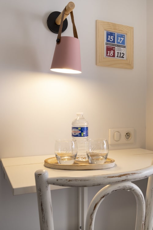 Chambre twin standard Hotel De Lion Sur Mer avec lampe murale rose, verres d'eau et calendrier sur mur blanc