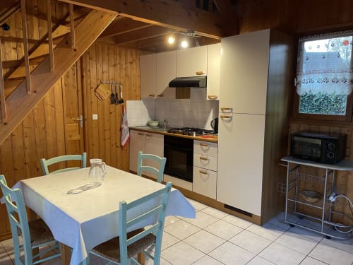 Cuisine-salle à manger chaleureuse avec poutres en bois, chaises bleues, cuisinière à gaz et meubles crème aux Gîtes Les Rainettes