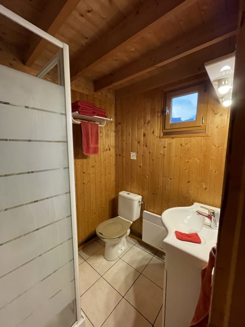 Salle de bain en bois avec toilettes, lavabo, douche et serviettes rouges au gîte Les Rainettes à Vienne-en-Bessin