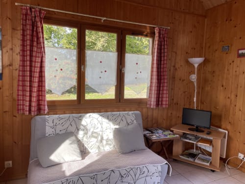 Chambre lumineuse du Gîtes Les Rainettes avec canapé blanc, vue sur jardin, murs en bois et télévision