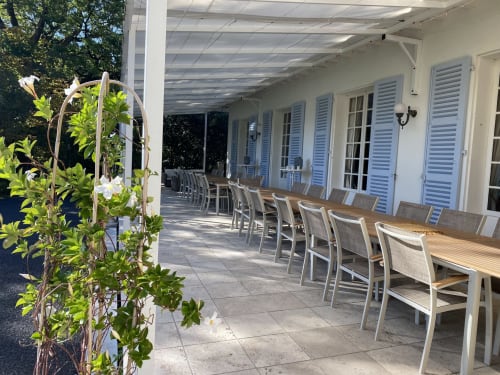 Terraza cubierta con mesas y sillas de comedor en el Domaine de Bize en Mirepoix, contraventanas blancas y flores trepadoras visibles