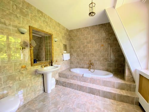 Baño de lujo en Domaine de Bize con bañera jacuzzi empotrada, lavabo pedestal, herrajes dorados y paredes alicatadas