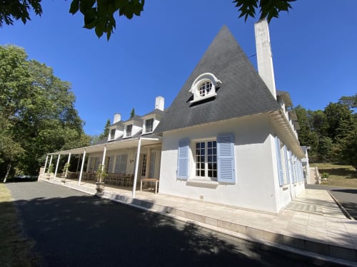 Cottage blanco con tejado mansarda y contraventanas azules en Domaine de Bize, un lujoso alojamiento rural en Mirepoix, Ariège, Francia