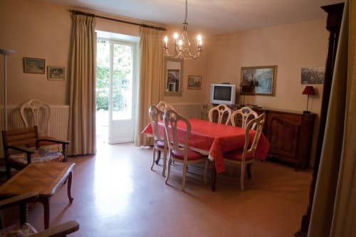 Élégante salle à manger du gîte La Maison de Lise à Figeac avec nappe rouge, chaises en bois, lustre et vue sur le jardin