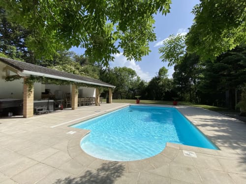 Piscine du Domaine de Bize à Mirepoix avec terrasse en pierre, pavillon, et parc ombragé sous ciel dégagé