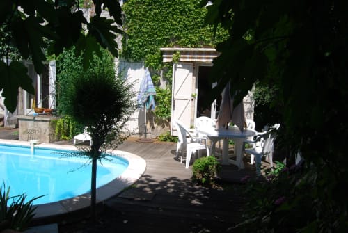 Zone piscine et patio du gîte Chambres d'hôtes Les Pratges à Figeac, avec bâtiments couverts de lierre et espace détente blanc.