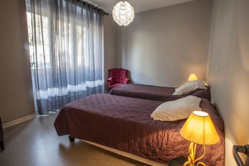 Chambre aux Chambres d'hôtes Les Pratges à Figeac avec lits jumeaux, literie bordeaux, luminaire suspendu et voilages