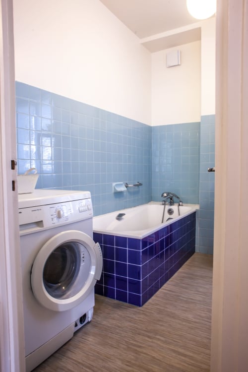 Salle de bains moderne avec lave-linge, baignoire carrelée bleue et parquet clair au gîte Les Pratges à Figeac