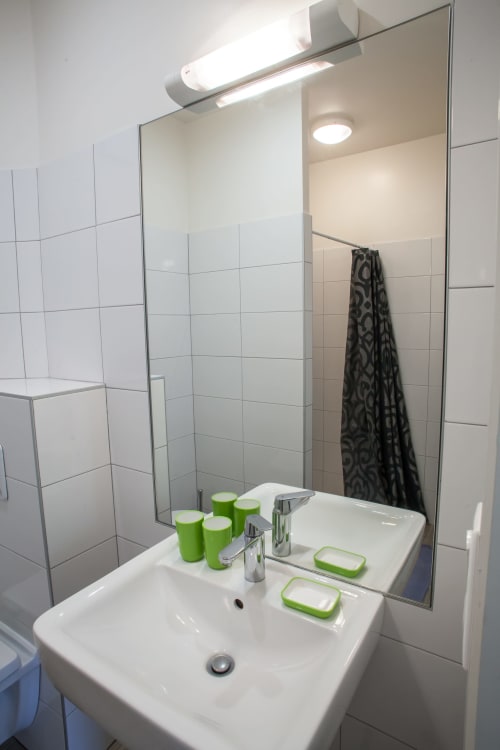 Salle de bain moderne du gîte Les Pratges à Figeac : lavabo blanc, miroir, accessoires verts et douche