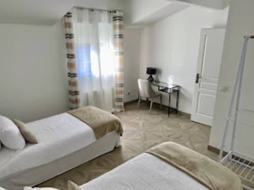 Bright twin bedroom with white beds, striped curtains, and garden view at Domaine de Bize Mirepoix, Ariège