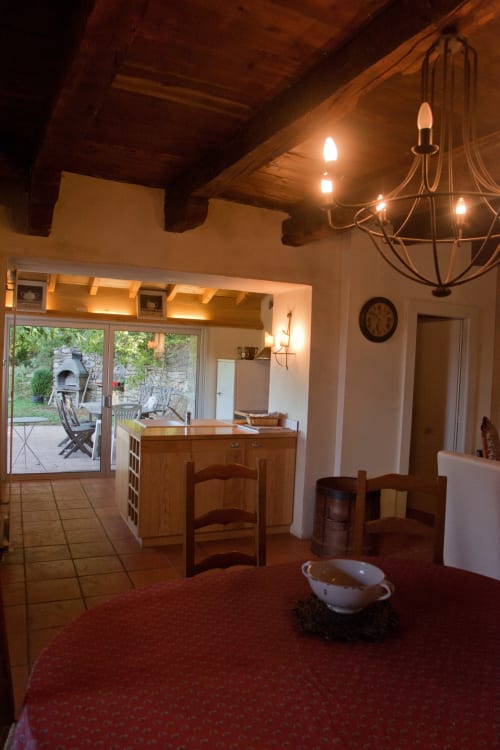 Chaleureuse salle à manger du gîte Les Pratges à Figeac avec poutres apparentes, lustre et vue sur le jardin