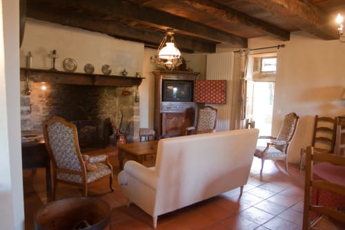 Salon rustique avec cheminée, canapé blanc, fauteuils à motifs et poutres apparentes aux Chambres d'hôtes Les Pratges