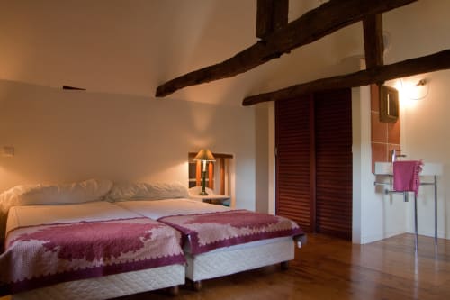Chambre spacieuse avec poutres apparentes, literie bordeaux et équipements modernes aux Chambres d'hôtes Les Pratges