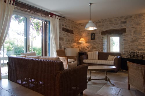 Salon rustique en pierre avec sièges en osier, cheminée et vue sur le jardin aux Chambres d'hôtes Les Pratges, Figeac