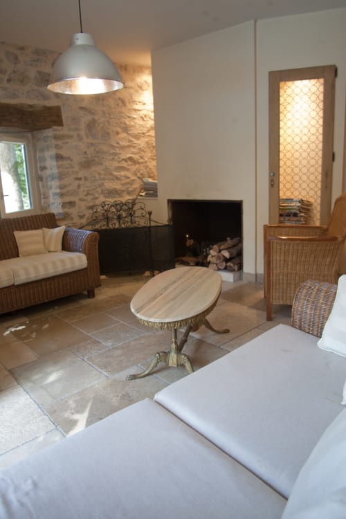 Élégant salon du gîte Chambres d'hôtes Les Pratges avec cheminée, mobilier en rotin et murs en pierre