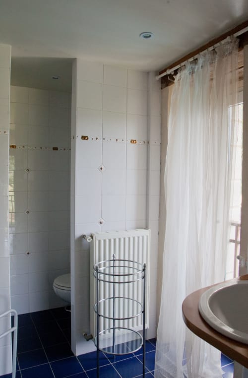 Salle de bain moderne aux carrelages blancs, douche pluie, radiateur chauffant et voilages légers à la Grange d'Andressac
