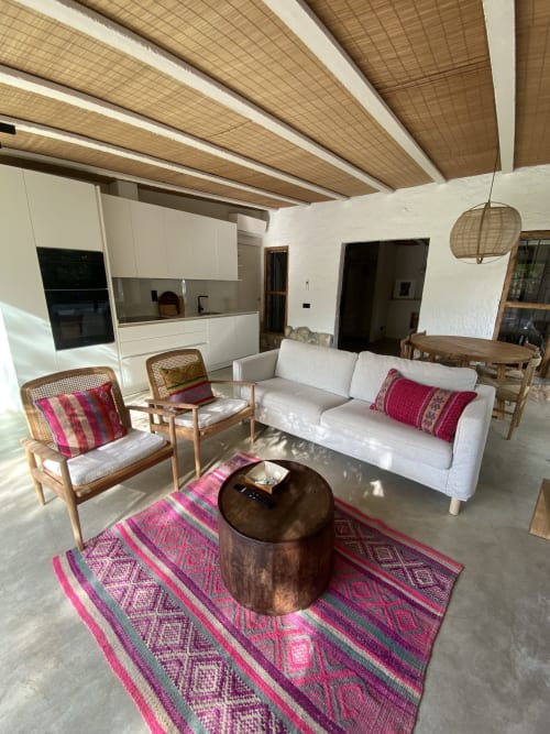 Moderna sala de estar de villa en BondBeach Village con sofá blanco, sillas de ratán, vigas de madera y geométricos coloridos