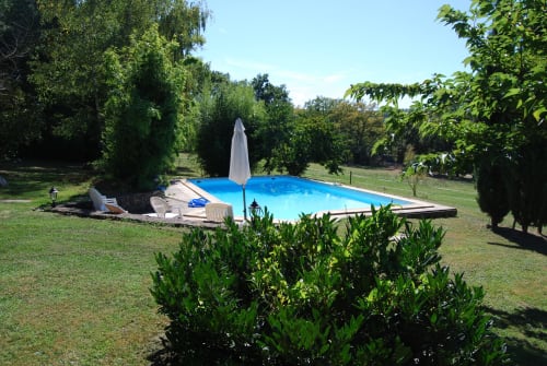 Piscine bleue avec parasol entourée de pelouses vertes et d'arbres au gîte Les Pratges à Figeac