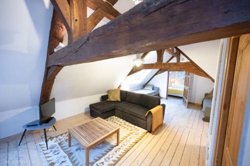 Salon mansardé à la Villa République Normandie avec poutres apparentes, canapé sombre et lumière naturelle à Caen