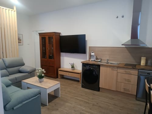 Moderno apartamento en Ávila con sofá gris, cocina integrada, televisor de pantalla plana y muebles de madera