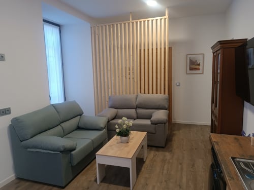 Salón moderno en Ávila con sofá verde, sillón marrón, mesa de madera y persianas verticales.