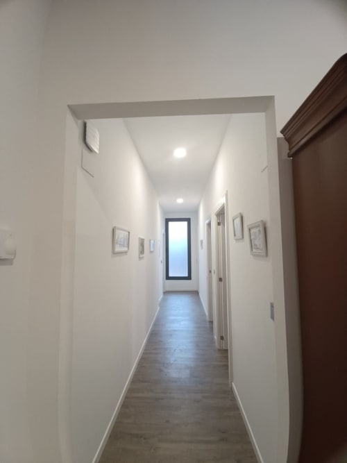 Luminoso pasillo en Apartamentos Turísticos Ávila con paredes blancas, pisos de madera oscura y cuadros enmarcados