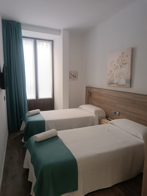 Dos camas individuales con ropa de cama verde y blanca en una habitación de hotel luminosa en Apartamentos Turísticos Ávila, con cabecero de madera y