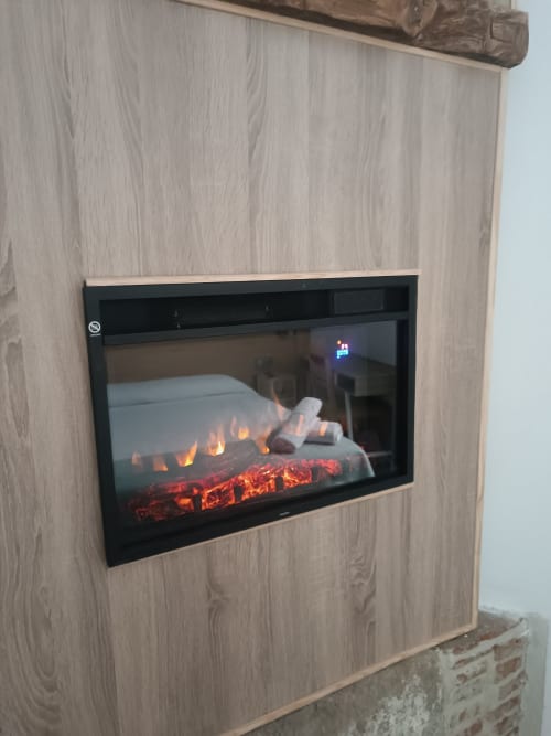 Chimenea eléctrica moderna con efecto de llama integrada en pared de madera clara en apartamento de Ávila