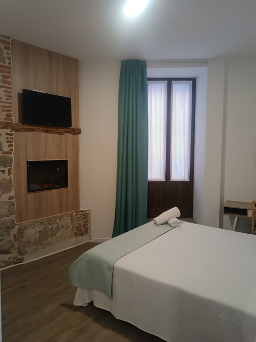 Moderna habitación en Apartamentos Turísticos Ávila con TV de pantalla plana, chimenea y vistas a la ciudad desde el balcón