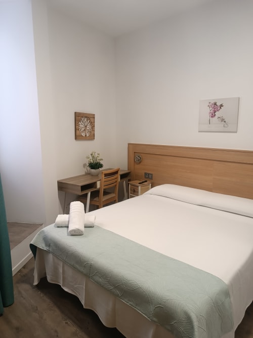 Habitación moderna en Apartamentos Turísticos Ávila con escritorio de madera, ropa de cama blanca y cuadros de vistas de la ciudad