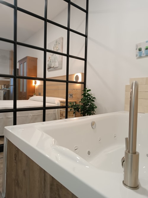 Baño moderno con bañera de inmersión blanca y mampara de vidrio con marco negro en Apartamentos Turísticos Ávila, vista del dormitorio