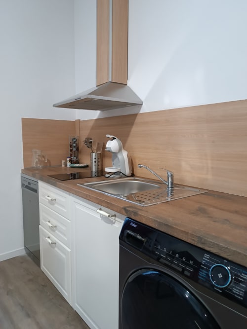 Cocina moderna en apartamento de Ávila con encimera de madera, armarios blancos, fregadero de acero inoxidable y lavadora negra