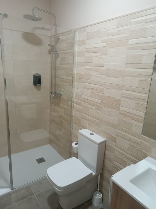 Moderno cuarto de baño con ducha de efecto lluvia, inodoro y paredes de azulejos beige en Apartamentos Turísticos Ávila