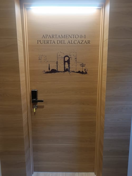 Puerta del Apartamento 0-1 Puerta del Alcázar en Apartamentos Turísticos Ávila con diseño de madera e ilustración del castillo del Alcázar