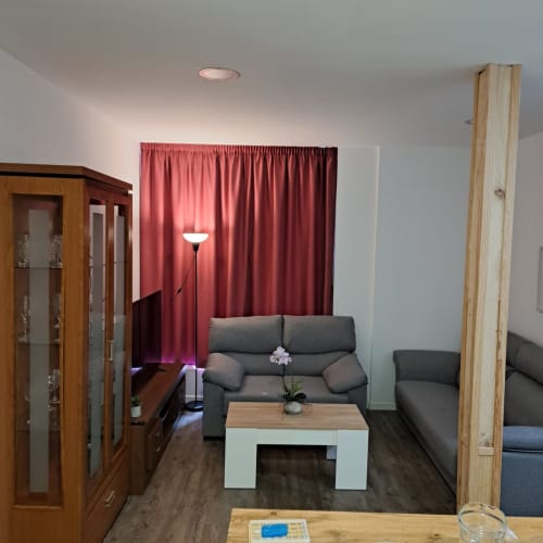 Salón moderno de apartamento con sofá gris, mesita blanca, cortinas rojas, mueble de madera y piso de parqué en Ávila.