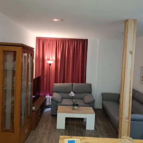 Sala de estar moderna en Ávila con sofá gris, mesita de madera, cortinas rojas y vistas a la ciudad