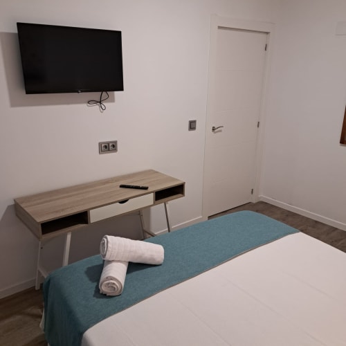 Habitación moderna en Apartamentos Turísticos Ávila con televisor de pantalla plana, escritorio, toallas enrolladas en la cama y puerta blanca