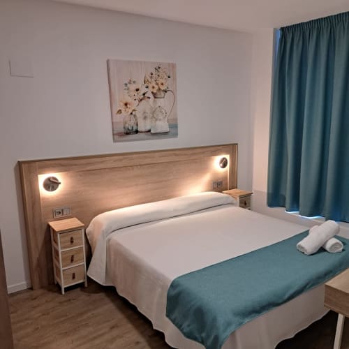 Dormitorio moderno en Apartamentos Turísticos Ávila con cama de marco de madera, ropa de cama blanca, detalles en azul verdoso y arte floral en la pared